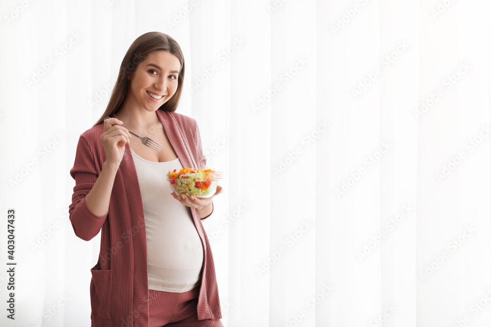 Nutrition During Pregnancy. Smiling Pregnant Lady Eating Fresh Vegetable Salad Near Window Nutrition During Pregnancy. Smiling Pregnant Lady Eating Fresh Vegetable Salad Near Window