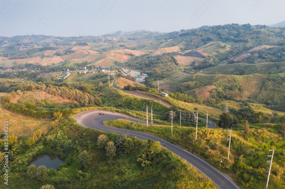 Scenery of Curved asphalt road with electric pole on green hill in countryside