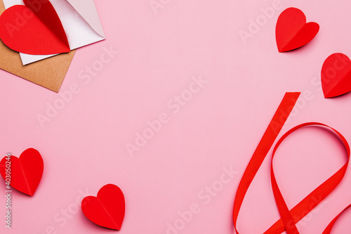 Valentine's Day pink background. Flat lay of paper hearts envelopes and valentines with red ribbon for hand made gift. Mother's Day concept. Greetings. Copy space, top view.
