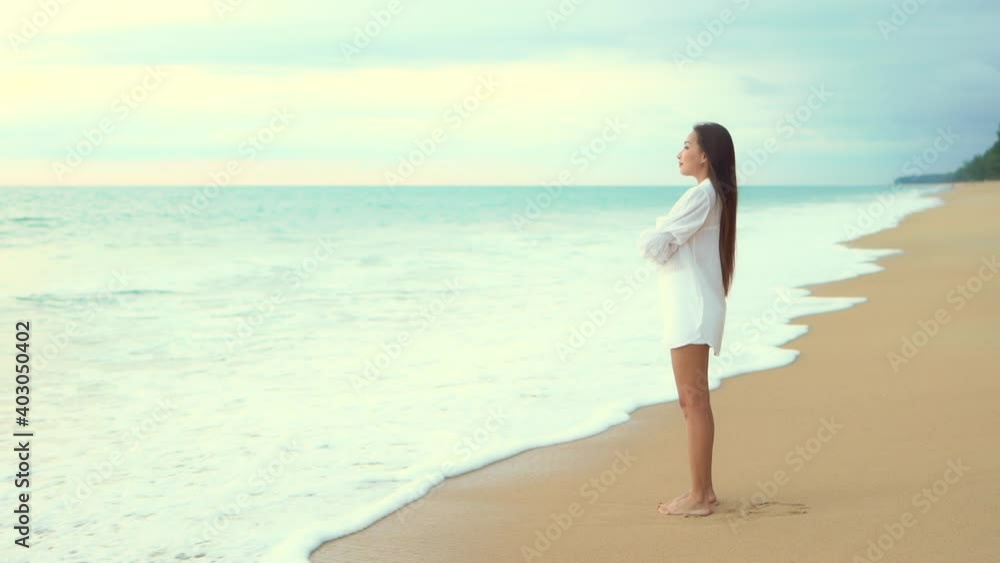 A pretty young woman stands on a sandy beach looking out on the incoming waves. Copy space A pretty young woman stands on a sandy beach looking out on the incoming waves. Copy space