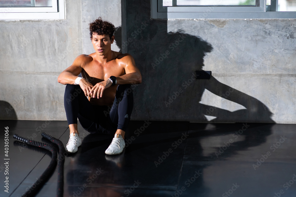 Obraz premium sportsman taking a break after training with battle rope at the gym sitting and drinking water at sport club. Fitness Healthy lifestye and workout at gym concept.