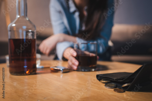 cropped view of alcohol-addicted woman taking glass of whiskey near wallet with coins, blurred background