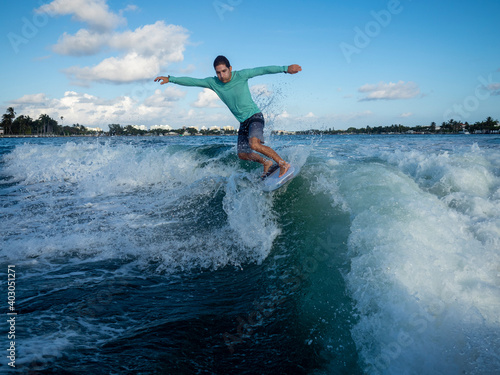 Athletic Man rides crest of wave with open arms, wearing shorts and long sleeve rashguard