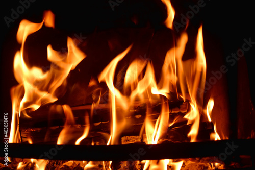 Closeup of dancing flames with dark background of burning wooden logs in fireplace, warming light in Christmas holidays