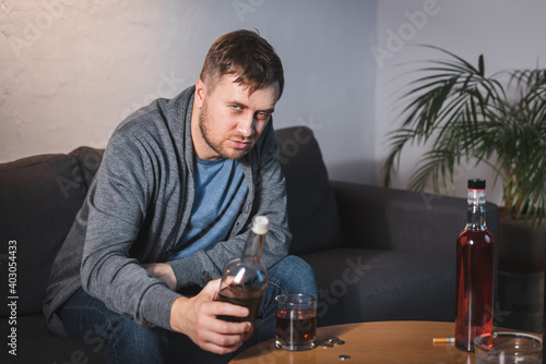 Fényképezés drunk man looking at camera while holding bottle of whiskey at home