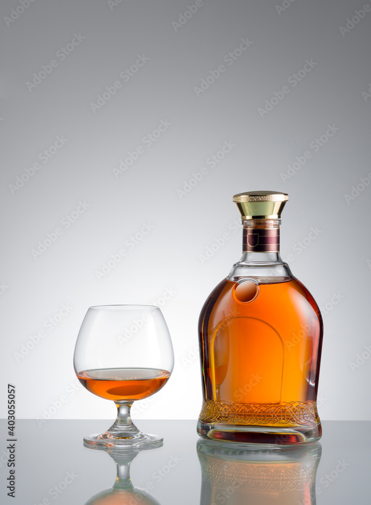 view of glass of cognac and a bottle aside on grey background. view of glass of cognac and a bottle aside on grey background.