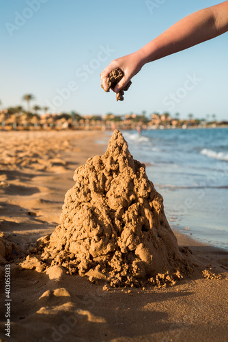 Sand castle made of sand by the hands of a child on the shore.Sea at sunset, white sand on the beach.Sunset sun, yellow light