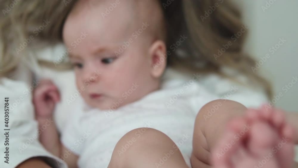 Close up curious baby lying on mommys legs, looking at camera with astonishment Close up curious baby lying on mommys legs, looking at camera with astonishment
