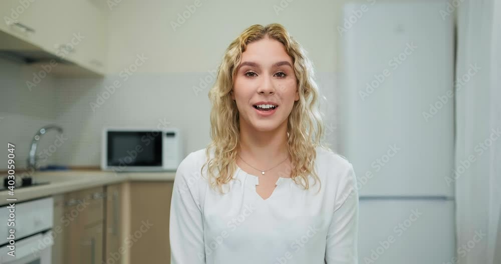 Smiling businesswoman with loose hair greets and talks to colleagues sitting in kitchen and looking into webcam at quarantine Smiling businesswoman with loose hair greets and talks to colleagues sitting in kitchen and looking into webcam at quarantine