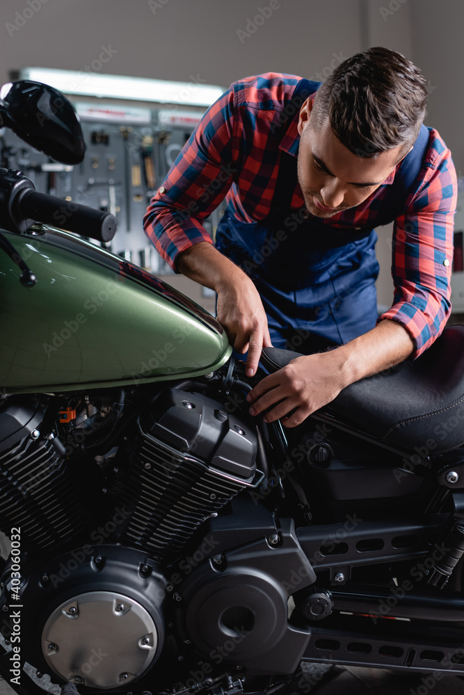 young mechanic pointing with finger while making diagnostics of motorbike in workshop