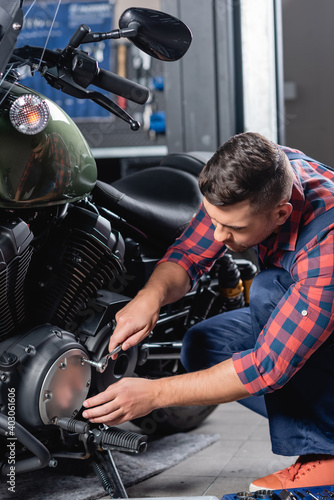 young mechanic unscrewing cap of motorcycle gearbox with socket wrench