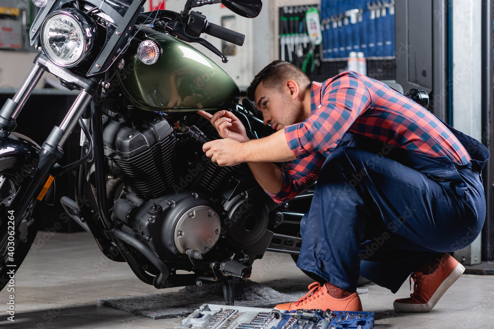 mechanic in overalls holding flashlight while making diagnostics of motorcycle