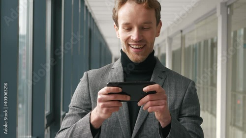 Close up bussisman is enjoying playing video game in smartphone standidng in office. Young man playing game on his smartphone while resting at work fun gameplay cyber gaming. photo