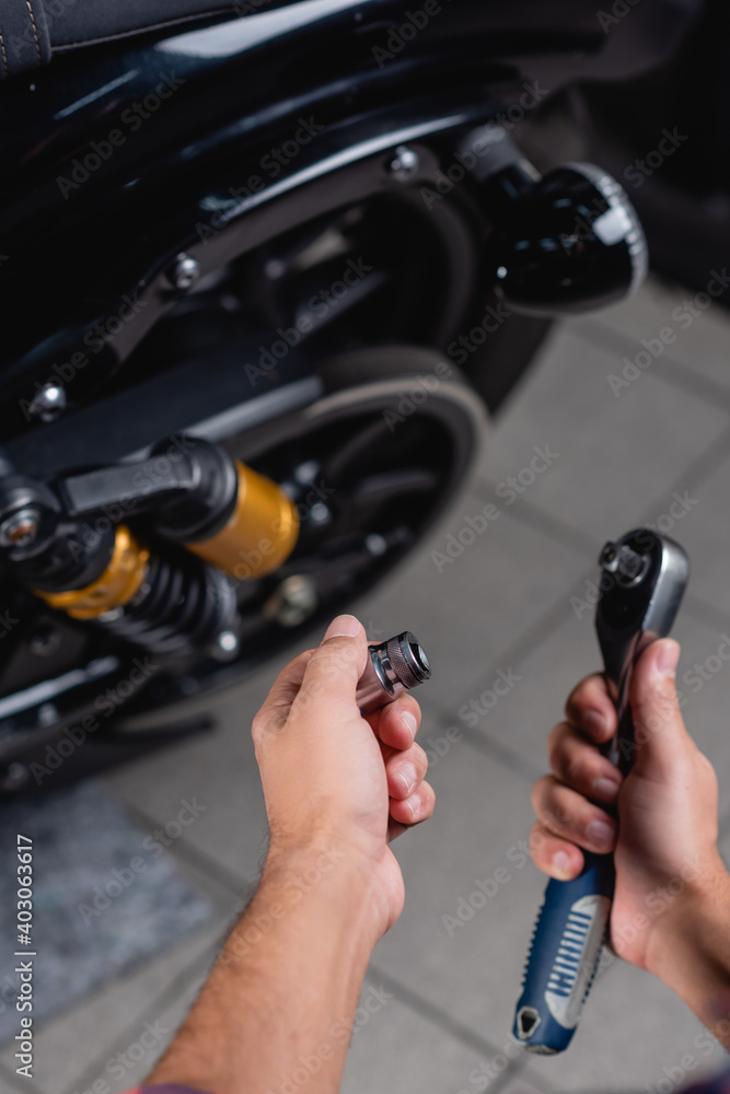 partial view of repairman holding socket wrench near motorbike on blurred background