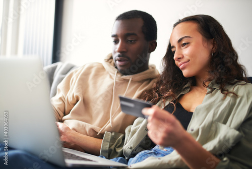 Young Couple At Home Sitting On Sofa Holding Credit Card Using Laptop To Shop Online