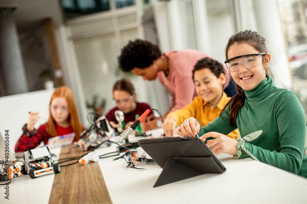 Obraz premium Happy kids with their African American female science teacher with laptop programming electric toys and robots at robotics classroom