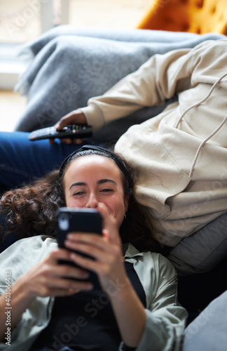 Overhead Shot Of Relaxed Young Couple At Home On Sofa Watching TV And Checking Mobile Phone
