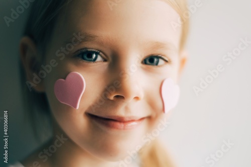 Close-up portrait of a girl wirh hearts on her face. Pink hearts on cheeks. Valentines concept. Portrait of a blonde child. 