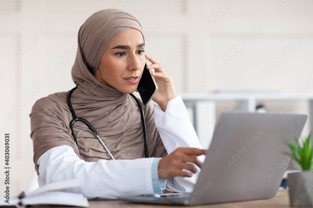 Female doctor looking at laptop screen and talking on phone Female doctor looking at laptop screen and talking on phone
