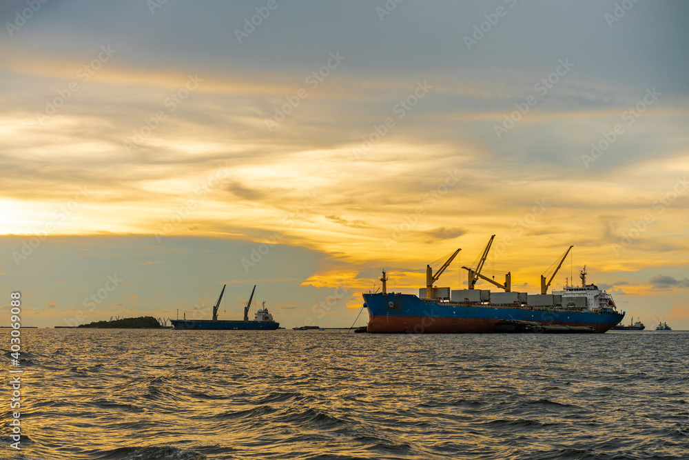 Large cargo ship for logistic import export goods anchor at sea in evening with golden sunset
