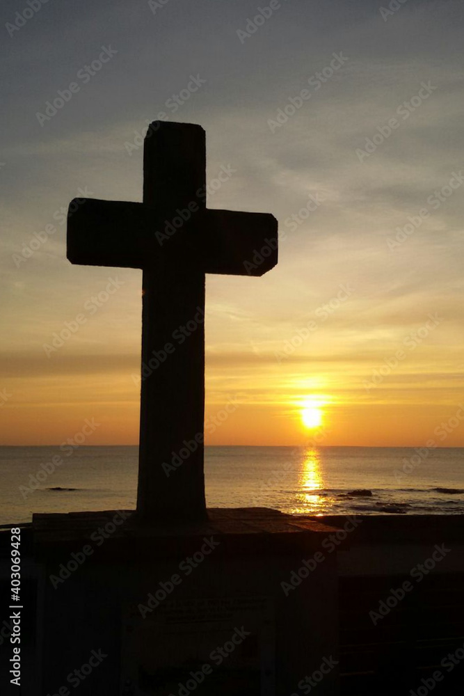 Silhouette of a Catholic cross in front of a sunset over the sea