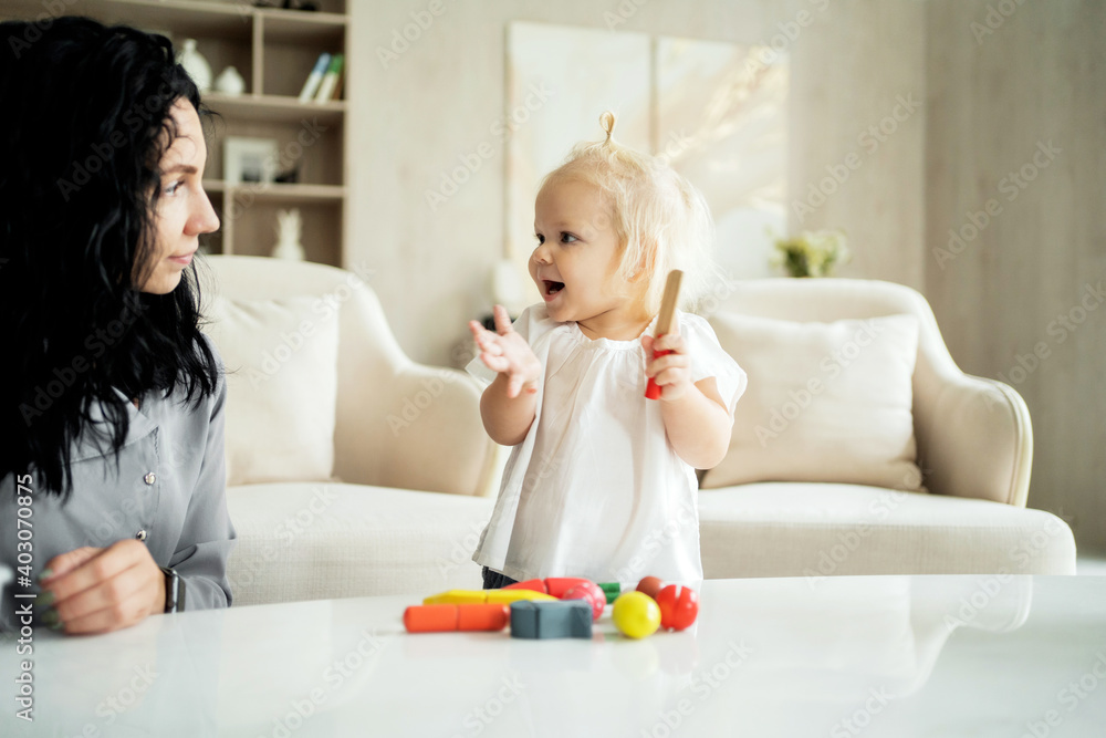 Spend time together. young family blonde daughter and brunette mother smiling playing children's games at home, hugging. They are dressed in stylish and comfortable clothes. Spend time together. young family blonde daughter and brunette mother smiling playing children's games at home, hugging. They are dressed in stylish and comfortable clothes.