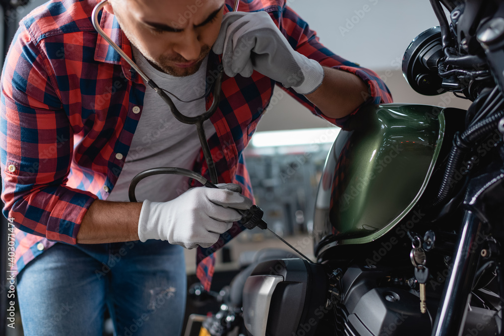 young mechanic in gloves checking motorbike engine with stethoscope young mechanic in gloves checking motorbike engine with stethoscope