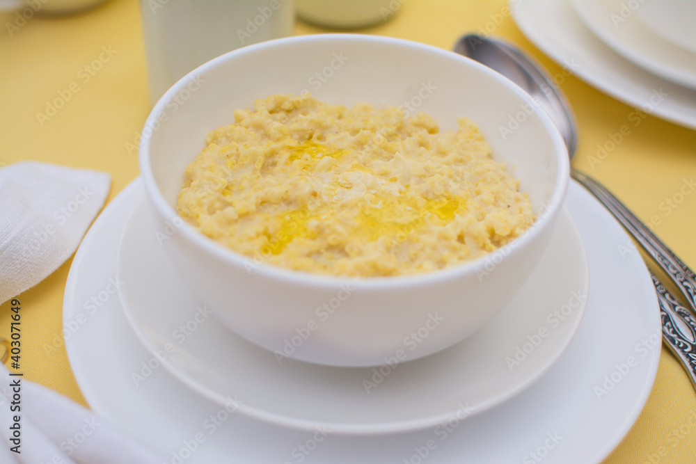 Millet porridge with butter in a white ceramic cup on a yellow tablecloth. Healthy eating. Healthy breakfast. Millet porridge with butter in a white ceramic cup on a yellow tablecloth. Healthy eating. Healthy breakfast.