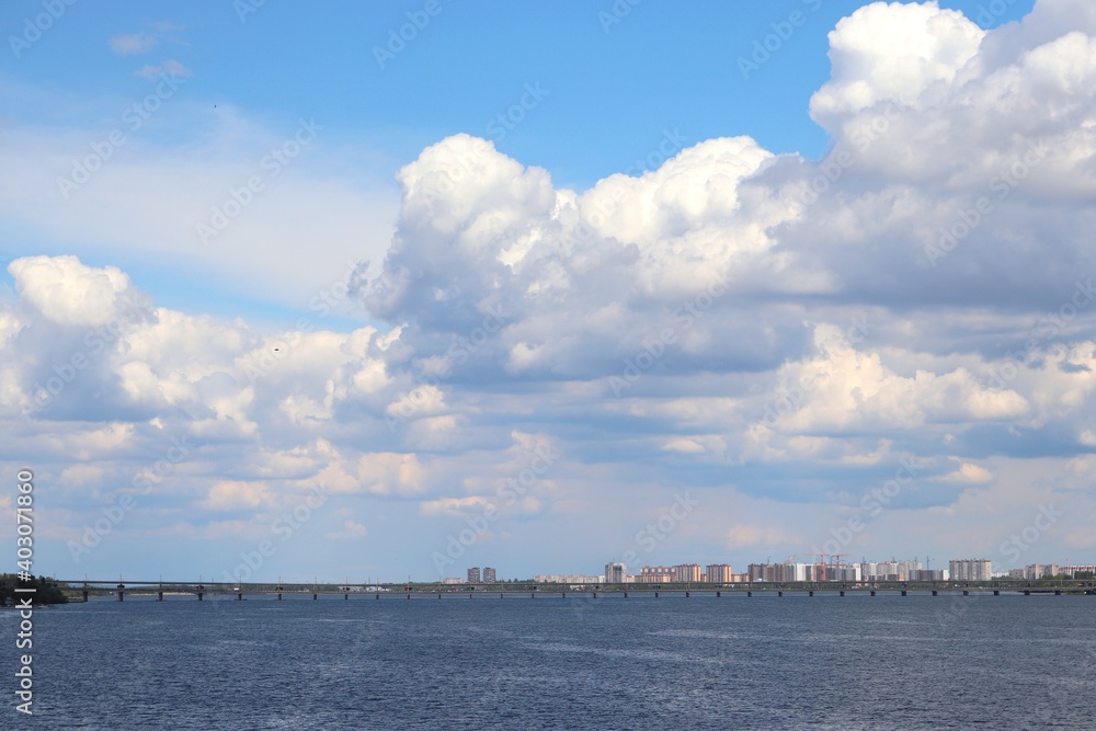 Voronezh city summer day urbanscape with the reservoir, blue sky with white clouds, and a bridge in the distance