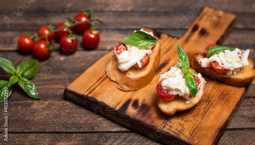 Bruschettas with stracciatella cheese cherry tomatoes and basil on wooden cutting board. Selective focus.