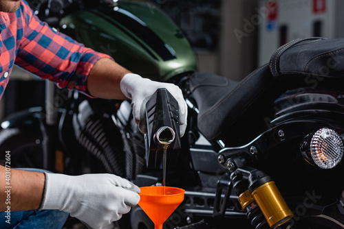 cropped view of mechanic pouring engine oil into funnel near motorbike on blurred background