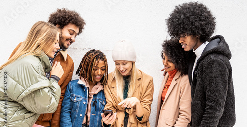 Fashionable multiethnic friends having fun together outdoors, looking at mobile phone.