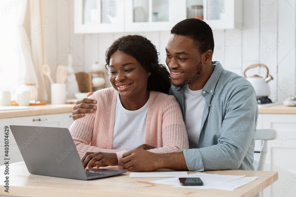 Smiling black couple with laptop on kitchen calculating bills, managing finances together Smiling black couple with laptop on kitchen calculating bills, managing finances together
