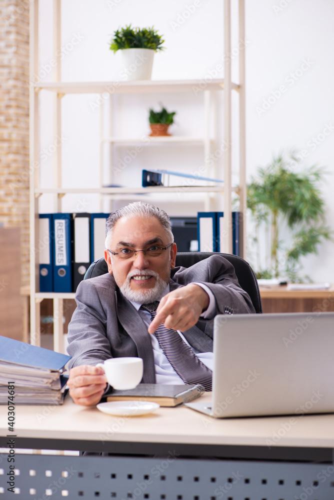Fototapeta premium Old male employee drinking coffee in the office