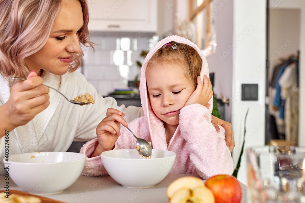 mother persuades her daughter to eat at least a spoonful of porridge, little girl is dissatisfied, sad, sits wants to sleep mother persuades her daughter to eat at least a spoonful of porridge, little girl is dissatisfied, sad, sits wants to sleep