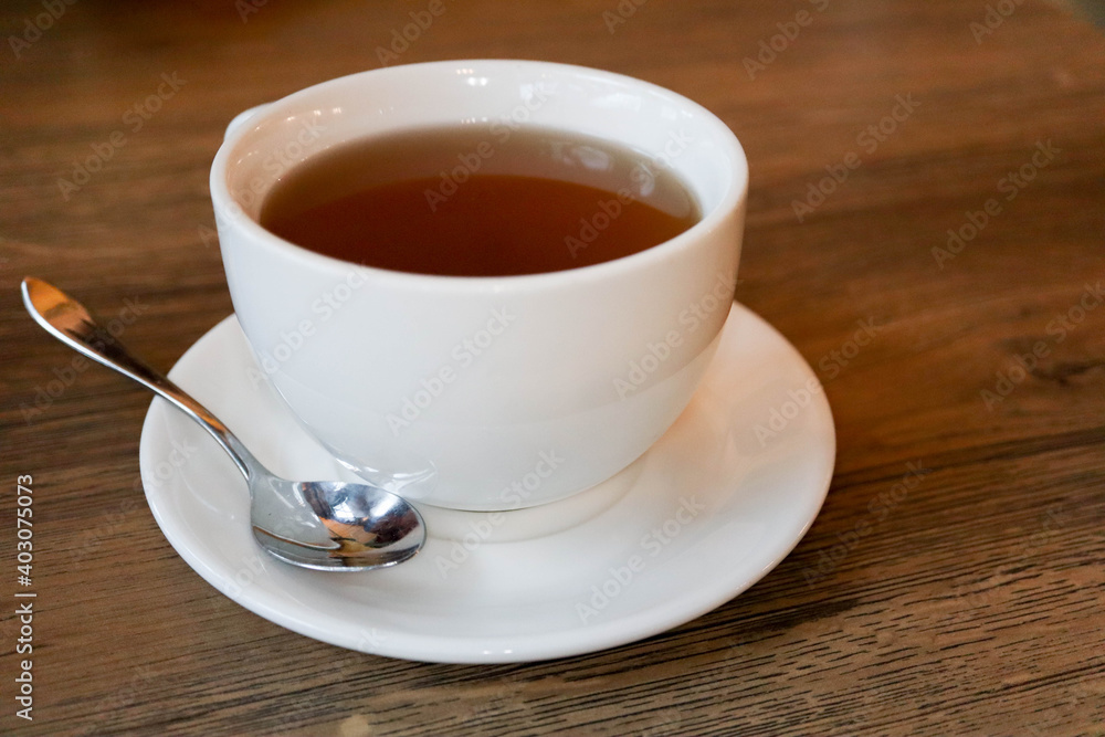 white cup of tea on plate with teaspoon on wooden table in cafe white cup of tea on plate with teaspoon on wooden table in cafe