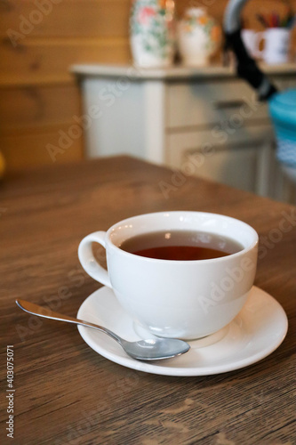 white cup of tea on plate with teaspoon on wooden table in cafe