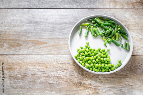 Green vegetables, peas and asparagus served on gray plate on wooden table. Rustic food background with copy space, flatlay.