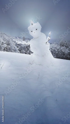 Bösartiger Schneemann, der verhängnisvoll die Arme ausbreitet, um jemanden zu fangen, oder zu umarmen. Angry snowman, bedrohlich und einschüchternd. Stöckchenarme und kalte Steinaugen. Lightglow snow.