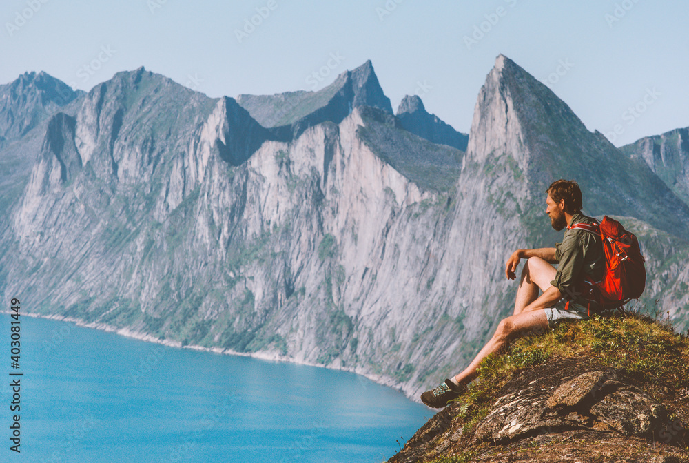 Man relaxing on cliff travel with backpack in Norway hiker enjoying mountains and fjord view adventure vacation outdoor active healthy lifestyle harmony with nature