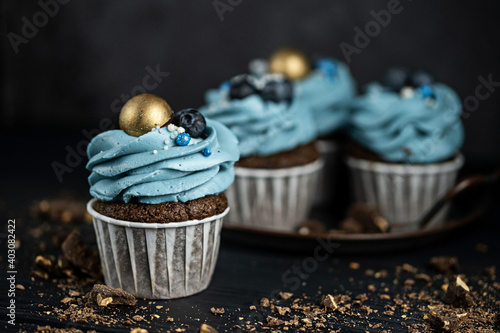 Several muffins or cupcakes with blue shaped cream and with blueberrieson at black table against a dark background. Rustic style copyspace.
