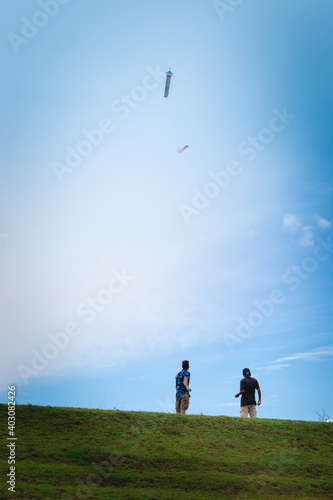 Two boys flying kites in a grass land mountain hill  blue bright sky