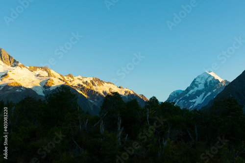 Sun at sunrise strikes snow-capped mountian peaks beyond silhouette of foreground hills of Southern Alps  Canterbury New Zealand.