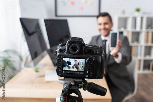 selective focus of digital camera near businessman holding smartphone with blank screen during video streaming on blurred background © LIGHTFIELD STUDIOS