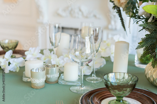 Luxury stylish bright light interior of sitting room. White walls decorated by ornament. Fireplace. Nobody inside room. Table setting by dishes  candles and flower bouquets.