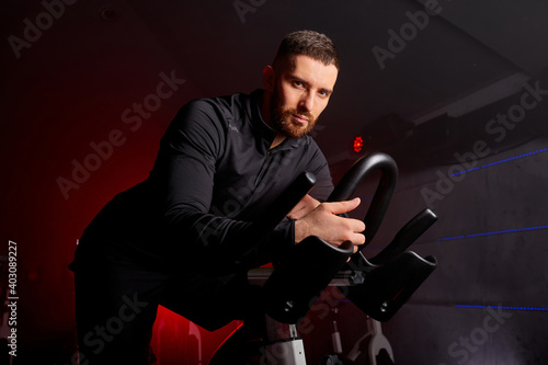 male in tracksuit sitting on stationary bike, posing, looking at camera. in dark studio room photo