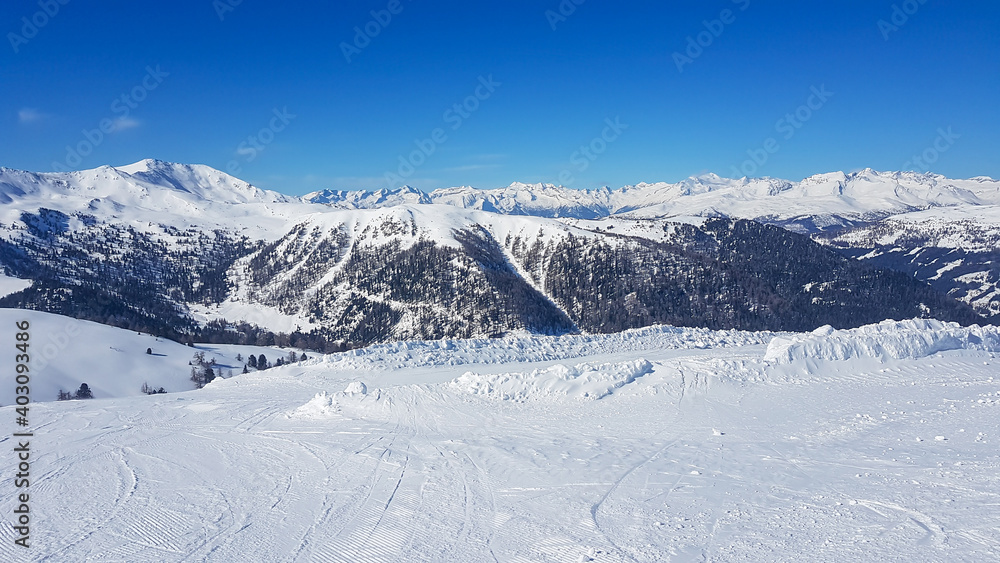 A panoramic view on the snow covered slopes of Innerkrems, Austria. The slopes are ready for skiing. Cloudless, blue sky. Many Alpine chains in the back. Winter wonderland. Fresh, powder snow.