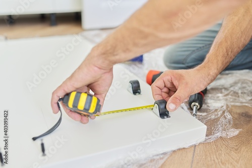 Assembling wood white furniture at home, carpenter's hands with tools and tape measure