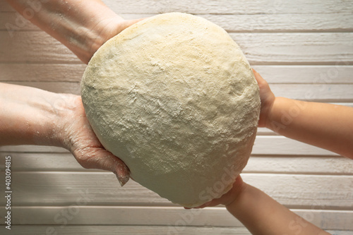 The hands of an old woman transmit bread dough to the small hands of a girl. The intergenerational connection. Different ages together. 