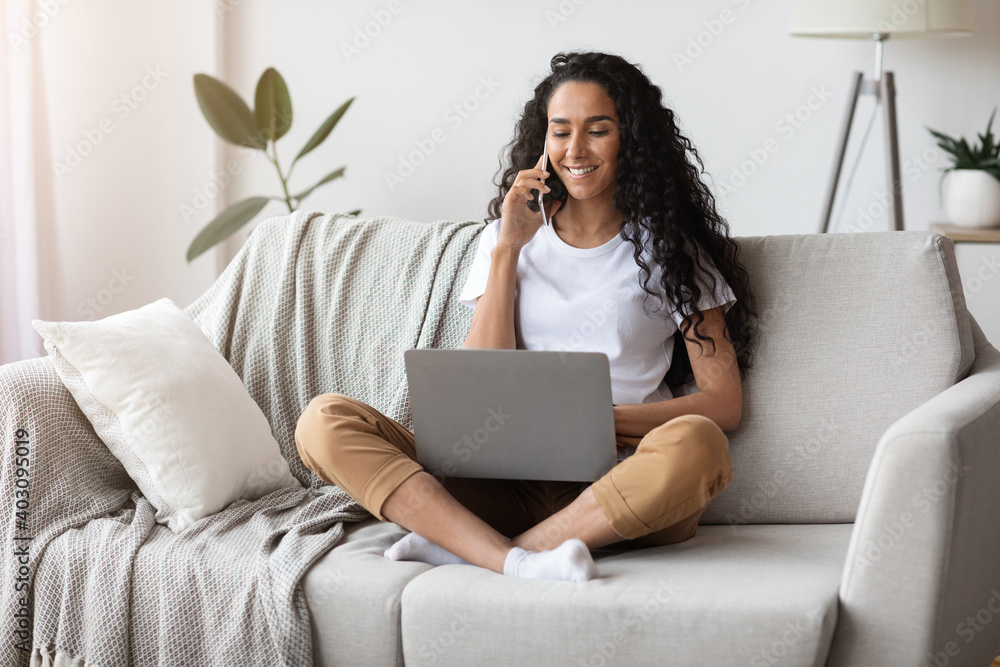 Naklejka premium Positive young lady working from home, using laptop and smartphone